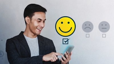 A person holding and interacting with a smartphone next to three emoticons—happy (yellow), neutral (gray), and sad (gray)—with a checkbox below each. Only the checkbox under the happy face is selected.